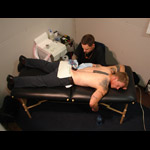 Jason Fitzpatrick lying prone on a bench being tattooed on the small of his back